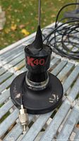 Close-up of the K40 antenna's magnetic base featuring the K40 logo, stainless steel antenna whip, and attached coaxial cable with connector.