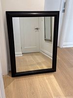 Full view of large rectangular mirror with custom dark espresso frame, positioned leaning against wall on light wooden floor.