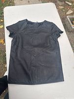 Black short sleeve leather top laid flat showing front design and shape
