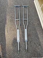 Pair of aluminum medical grade crutches lying on black asphalt showing height adjustment holes and rubber tips