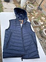 Navy blue hooded winter vest laid flat, showing front with zipper and hood.