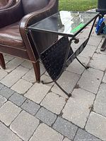 Full view of metal frame side table with glass top placed next to a leather armchair on stone patio.