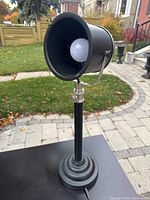 Front angle view of the black and silver Howin HXT0822 metal spotlight counter lamp showing conical shade with light bulb and stepped round base.