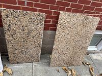 Both granite slabs standing against a brick wall showing their color and size difference.