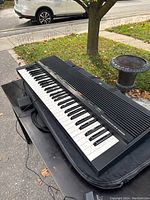 Full view of Yamaha YPR-9 portable piano keyboard on table outdoors showing keyboard and carrying bag underneath.