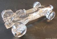 Perspectival image showing transparent crystal race car shape on a dark surface. Light reflections highlight contours and wheels.