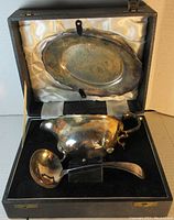 Silver gravy boat with attached underplate and matching ladle inside gift box with satin and velvet lining.