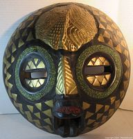 Full view of the carved round head sculpture with brass sheeting and bead inlay showing geometric and organic patterns.