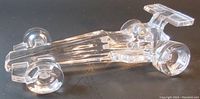 Top-down angled view of the clear glass Formula One race car paperweight highlighting the aerodynamic shape and details like the wheels and rear wing.