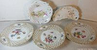Five porcelain dishes arranged on a surface showing three round pierced plates and two irregular shaped dishes including side/bone dish.