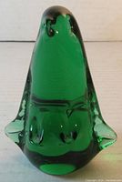 Front view of the green glass penguin paperweight showing the smooth surface, prominent rounded shape and flipper details.
