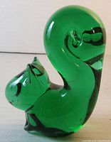 Front view of the green glass squirrel paperweight showing the rounded body and the curled tail with a smooth surface.