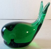 Side view of green glass whale paperweight showing curved body and upright tail fin