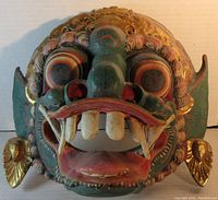 Front view showing detailed facial features and colors of the green and gold carved mask wall plaque