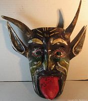 Front view of the mask showing the red tongue, facial paint, and wood root horns and ears.