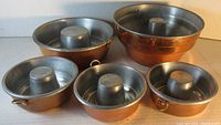 Set of five copper bunt pans of varying sizes, showing exterior copper and loop handles