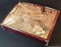 Set of four crystal cutting utensil rests arranged in original box with a gold cardboard liner featuring a white flower decoration and a background of plain dark surface.