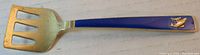 Full view of the serving fork showing the spatula-style fork head and blue enamel handle with fisherman and fish motif.