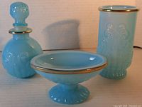 Photo of complete three piece baby blue milk glass vanity set with gold rim from Avon including perfume bottle, footed bowl, and cylindrical container