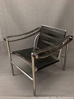 Front three-quarter view of chair showing chrome tubular frame, black leather sling seat and armrests.