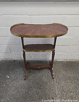 Front view of the small kidney shaped serving table with visible mahogany veneer and brass gallery on top shelf.