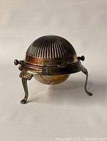 Closed view of vintage silver-plated roll-top butter dish showing ribbed domed lid and three ornate legs.