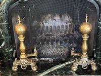 Pair of brass andirons placed in front of fireplace showing overall design and scale