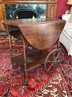 Full side view of the antique walnut tea wagon with both leaves folded down, showing large wooden spoked wheels and small caster wheels.