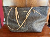 Front view of the Calvin Klein large tote bag showing signature CK monogram canvas and beige leather straps.