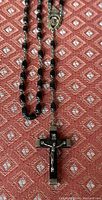 Full view of the rosary necklace laid out showing black polished ebony oval beads connected with silver chain and the crucifix at the end.