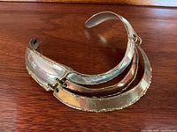 Front angle of the tri-coloured metal choker necklace showing silver, copper and brass curved overlapping bands with hammered texture.