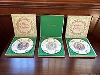 Three Royal Doulton Christmas plates in original boxes displayed open, showing the plates and festive box designs.