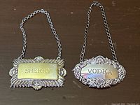 Both decanter labels for Sherry and Vodka lying side by side on a wooden surface.