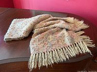 Full view of thick wool shawl laid on table with fringed ends visible