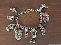 Full view of the gold-coloured charm bracelet showcasing the 10 detailed charms including a palette, hand, cuckoo clock, and golf bag charm