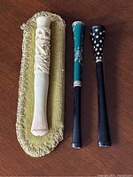 Lot of three vintage cigarette holders on gold padded stand, showing ivory carved piece and two black holders with decorative details.