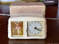 Front view of vintage Elg-Art ballerina alarm clock with original box behind. Shows clock face and ballerina figure.