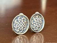 Close-up view showing the detailed raised Celtic knot design on the earrings' oval faces and the silver's lightly tarnished surface.