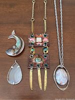 Five vintage handmade jewellery pieces shown on brown wood surface including two sterling silver pendants, an agate pendant, a mixed metal rectangular pendant with brass accents, and two oval pendants with white material.