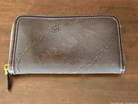 Front view of brown jacquard Prada wallet showing large woven logo and rope design with leather trim and zipper closure.
