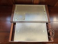 Top-down view of both vintage Salton Hotray food warming trays stacked, showing wood-framed bases and heating surfaces with patterned metal plates.