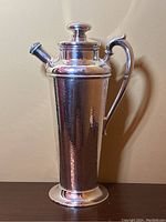 Full front shot of vintage silver plated cocktail shaker showing hammered texture, handle and lid.