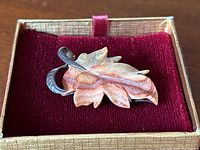 Photo of front face of a leaf-shaped brooch with carved agate in fall colors, set in sterling silver, placed on red velvet.