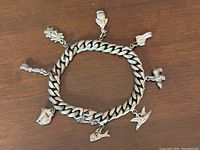 Full view of the vintage sterling silver animal charm bracelet showing solid curb link and seven attached animal charms, laid flat on wood.