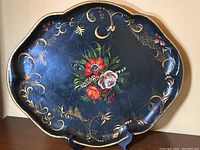 Full front view of the scalloped black metal tray showing the floral pattern and gold trim.