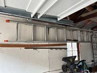 Full view of aluminum extension ladder hung on wall with orange end caps, showing two main ladder sections.