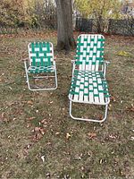 Both aluminum folding chairs outdoors on grass with autumn leaves, one a lounge chair and one a regular chair with wood armrests.