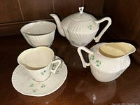 Photo showing the teapot, creamer pitcher, tea cup with saucer, and bowl arranged on wood surface.