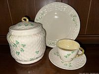 Full view of the biscuit jar, cup on saucer, and plate all showcasing the basket weave texture and shamrock decoration.