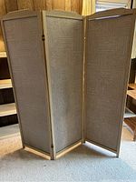 Full view of the vintage trifold room divider standing on carpeted floor with visible wooden frame and fabric panels featuring linear geometric patterns.